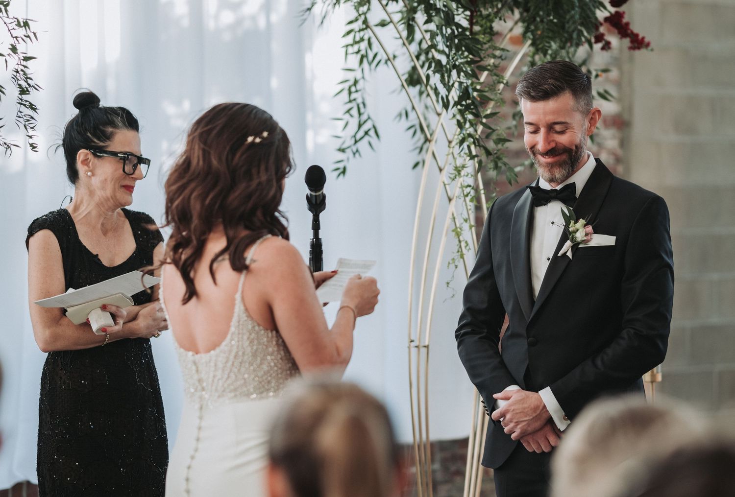 A wedding ceremony moment captured in an industrial venue with white draping and greenery.