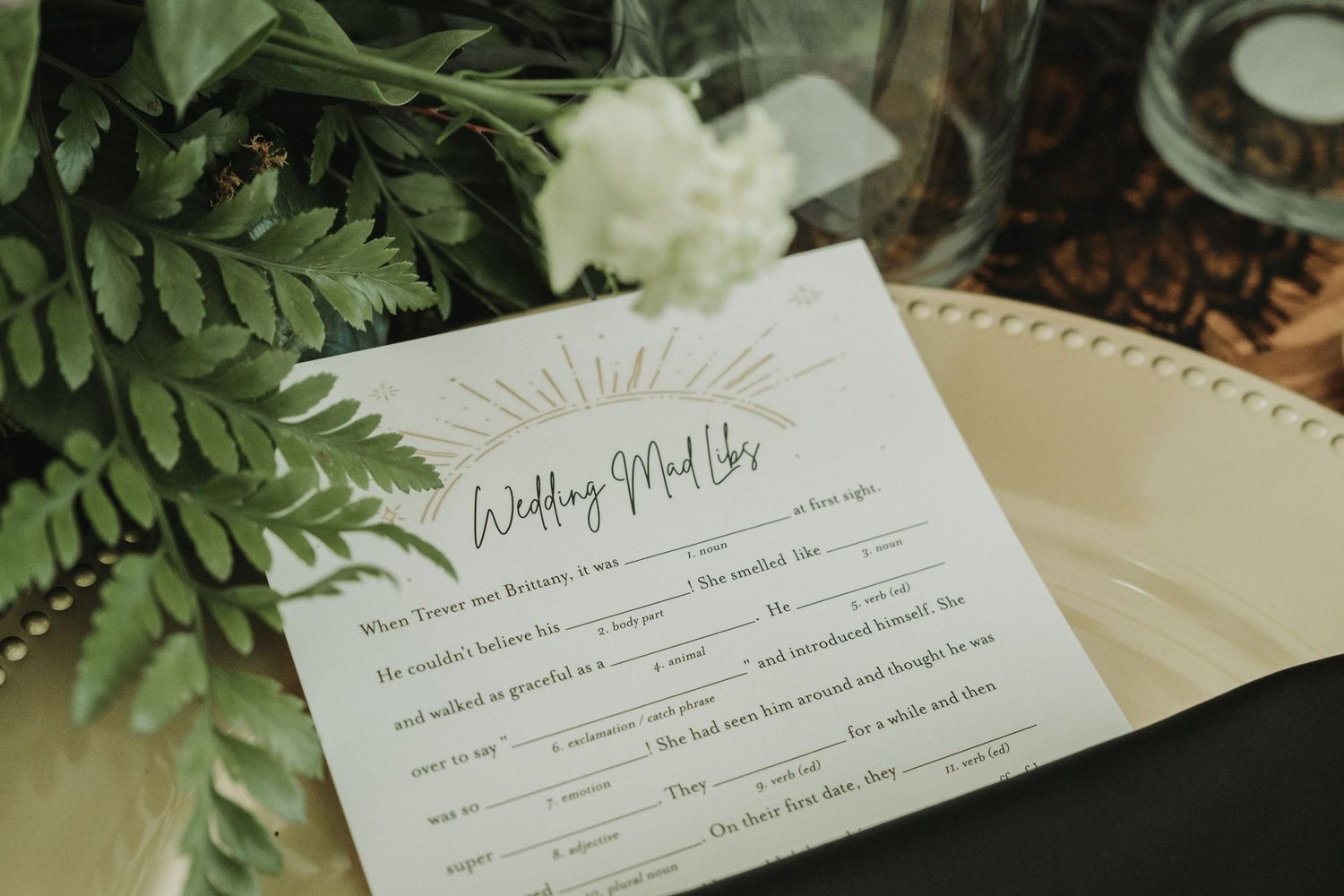 Wedding mad libs game card with ferns and floral decorations on cream colored plate.