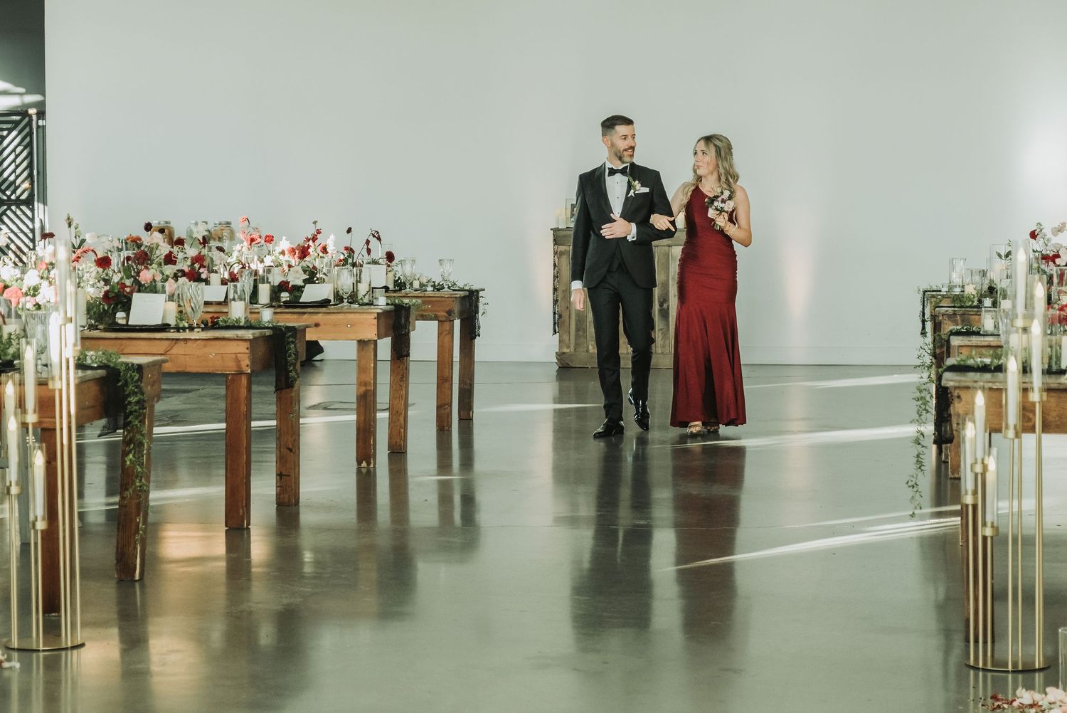 Modern wedding ceremony setup with wooden tables and floral arrangements in an industrial space.