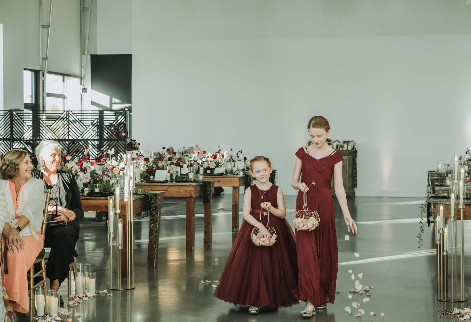 Wedding processional in burgundy dresses walking down aisle with floral decor.