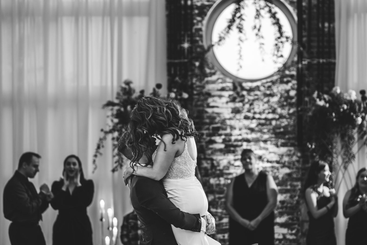 Black and white photo of a first dance at a wedding with decorative lighting.