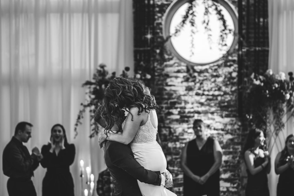 Black and white photo of a first dance at a wedding with decorative lighting.