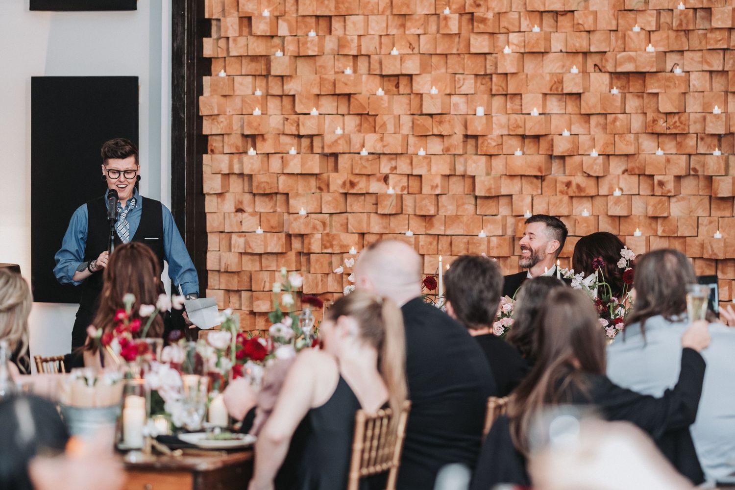 Speaker addressing wedding guests during reception dinner at modern venue.