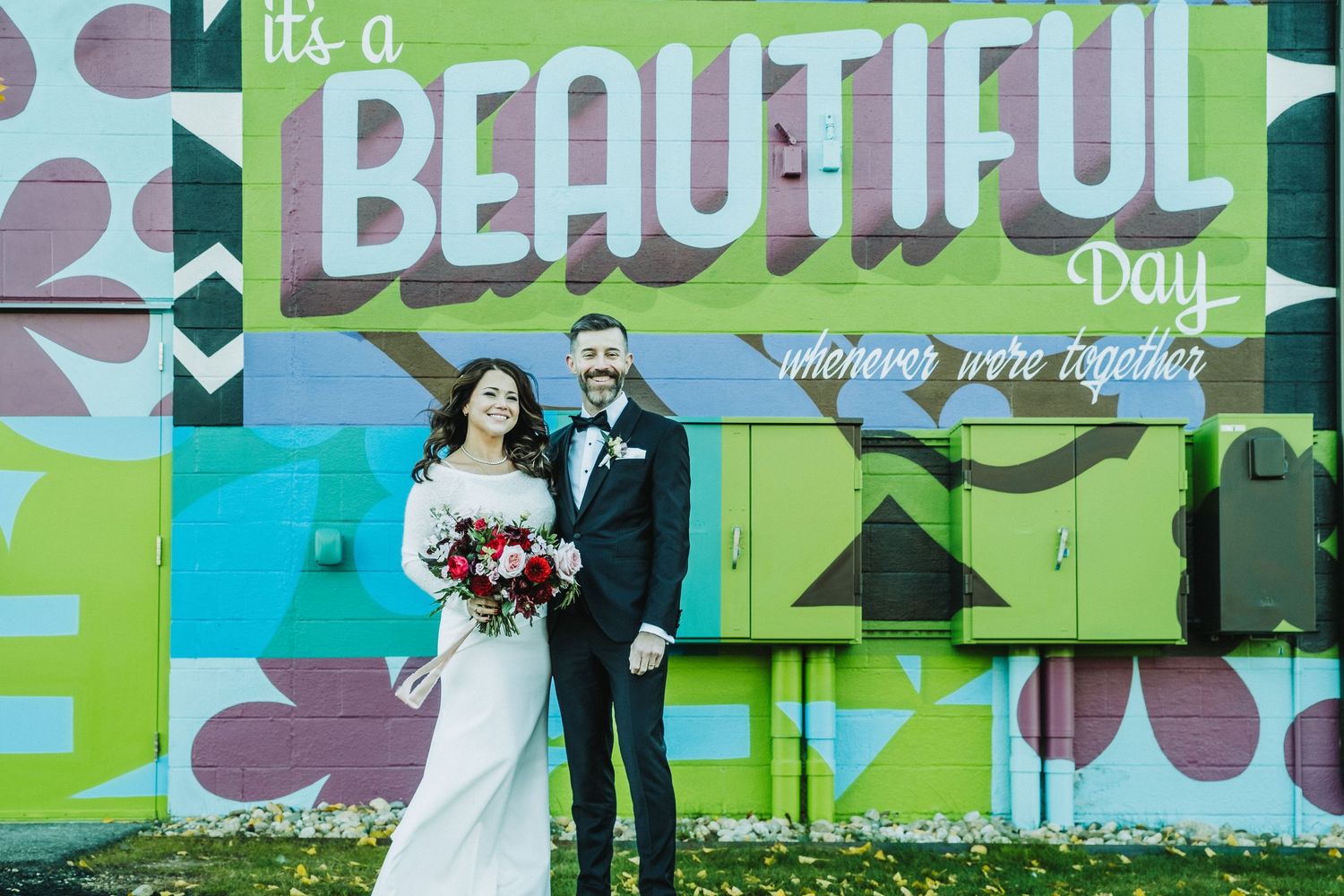 Wedding couple posed in front of colorful street art mural reading 'It's a Beautiful Day'.