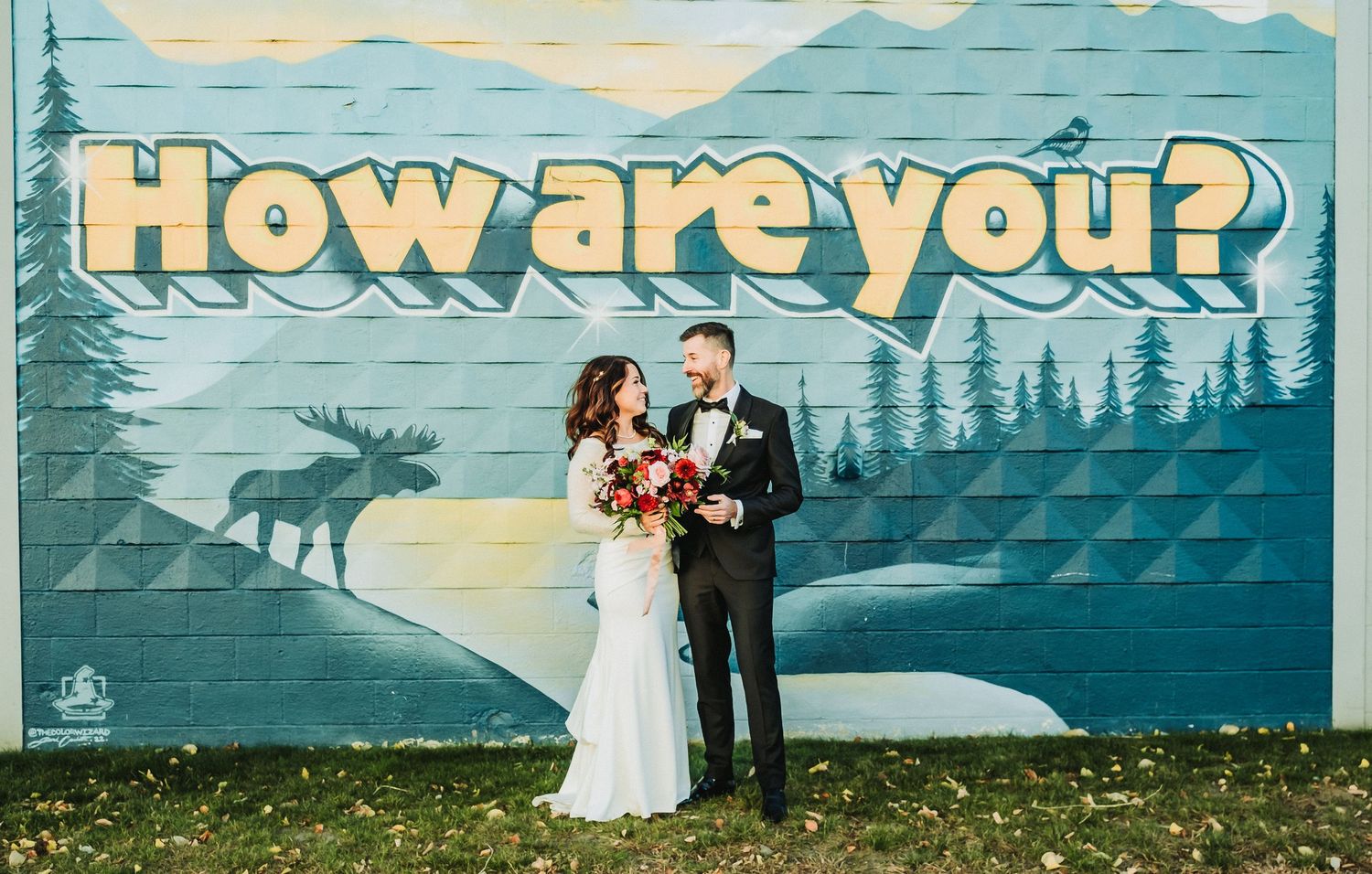 Wedding couple standing in front of retro-style mural with moose and forest landscape.