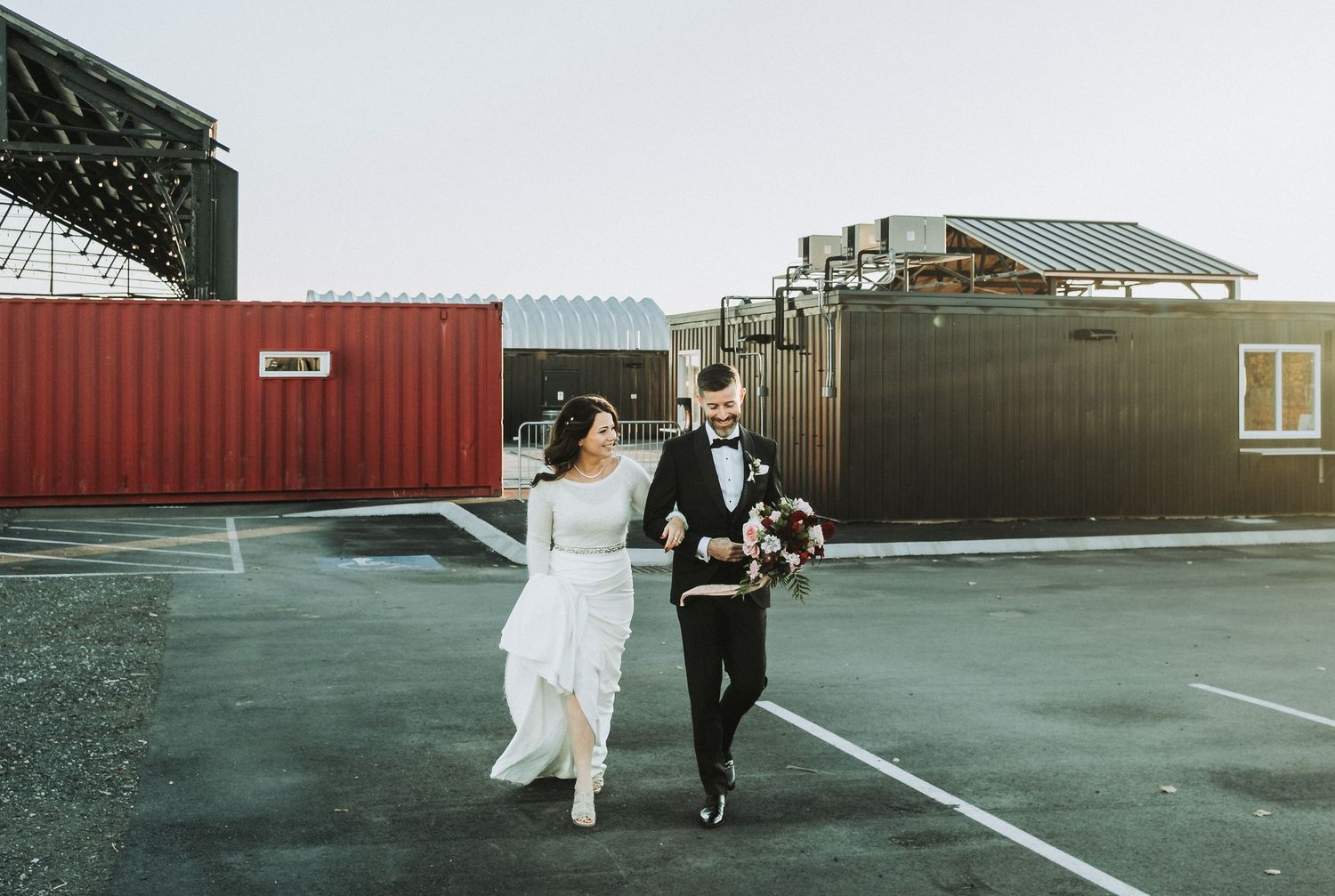 Couple running through industrial area with shipping containers in background.