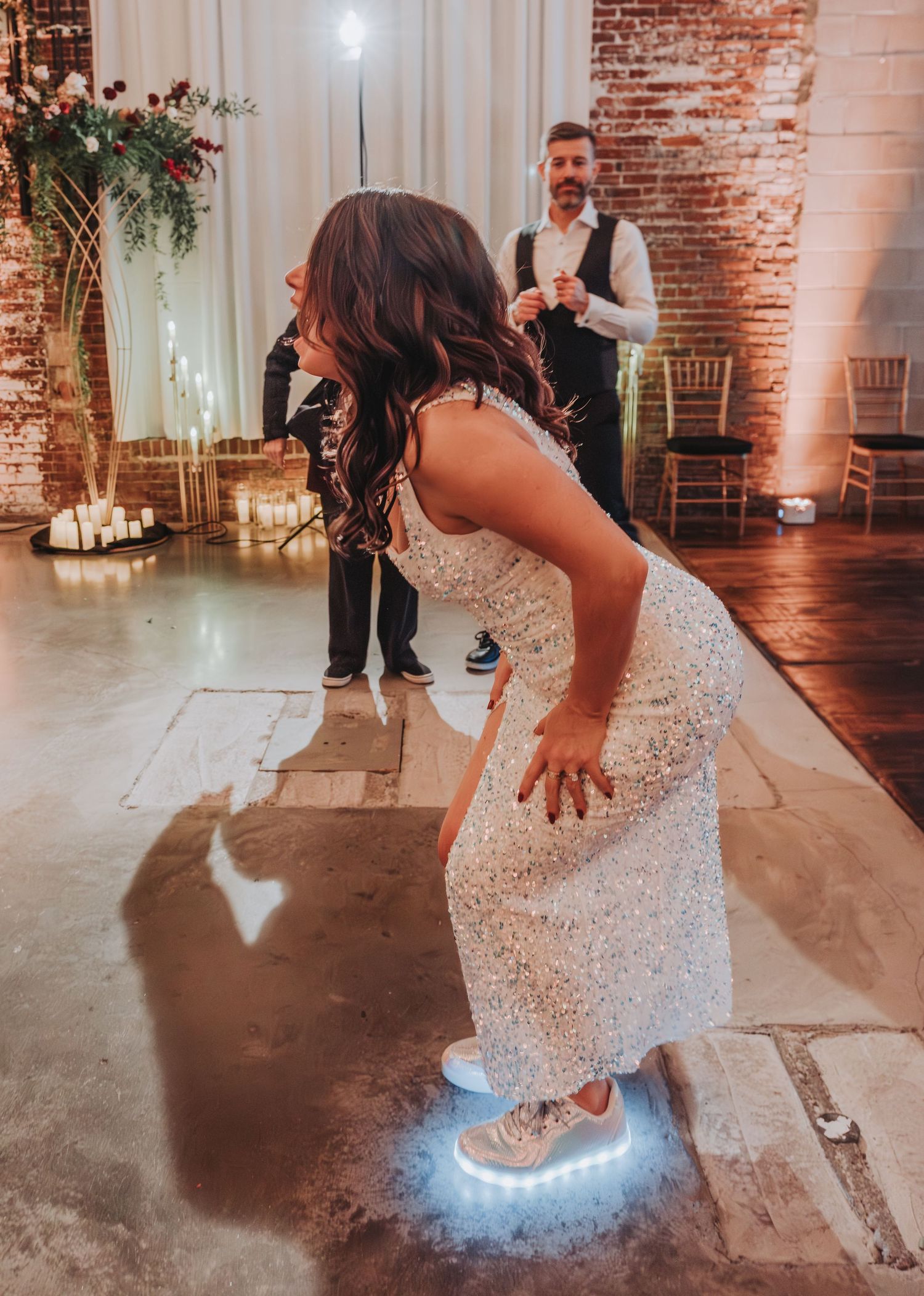 Person in white dress dancing with illuminated shoes on concrete floor.