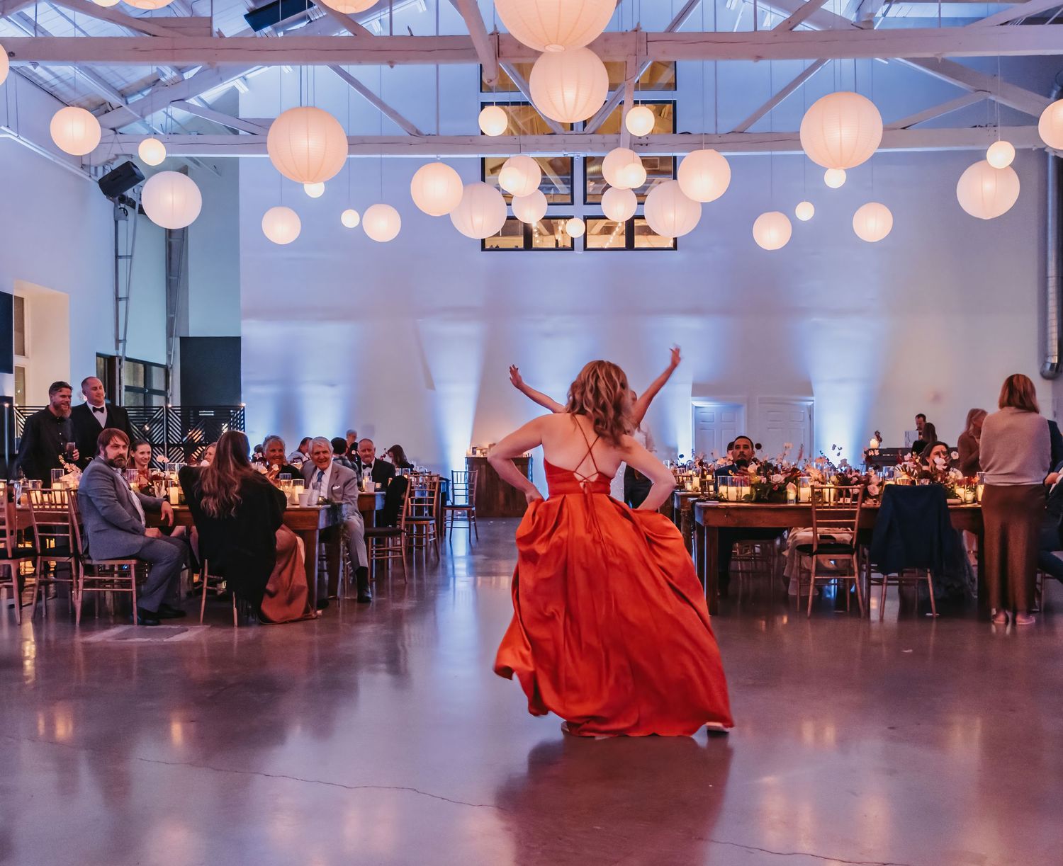 Dancing celebration at a wedding reception with white paper lanterns and industrial ceiling.