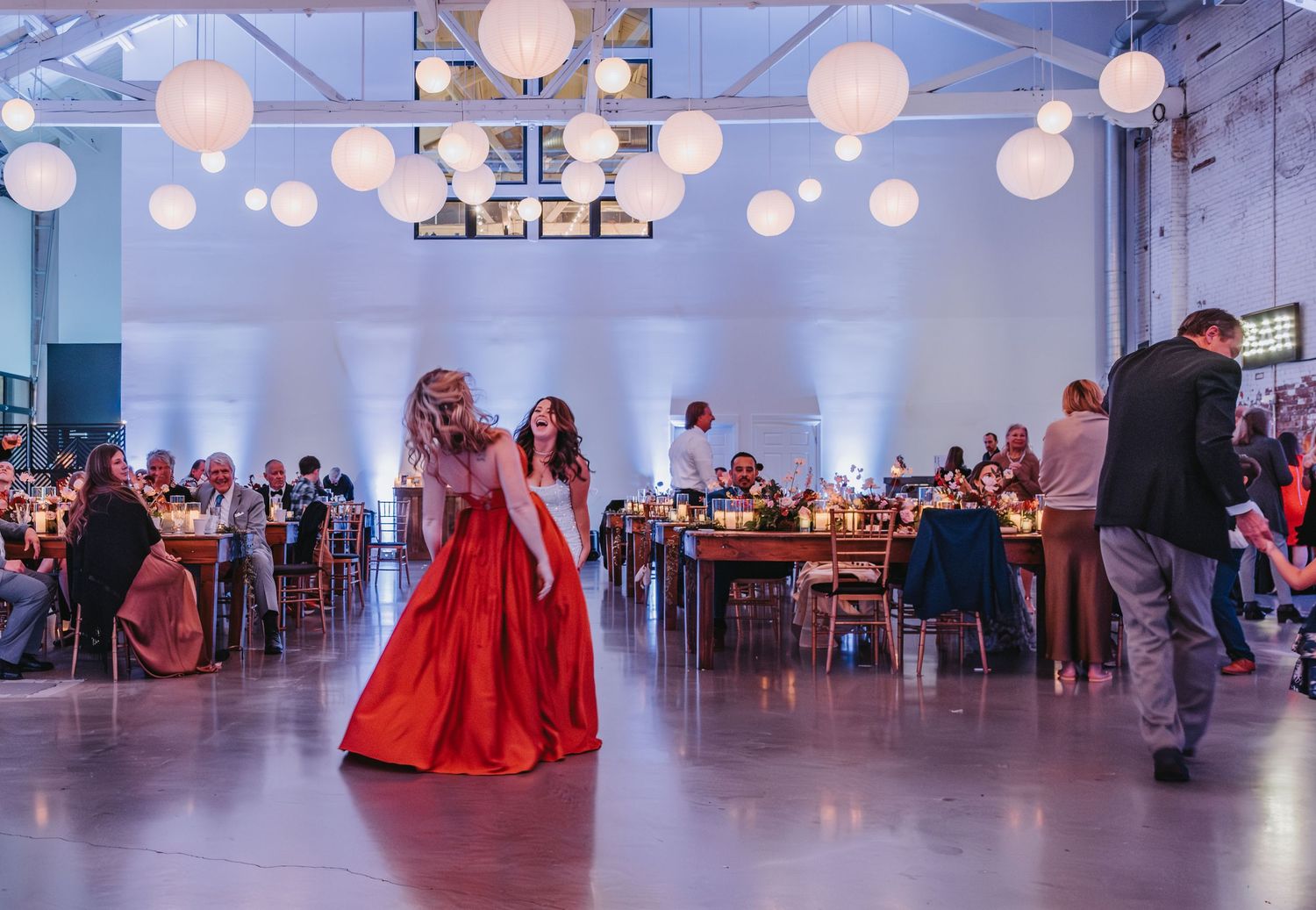 Wedding reception with stunning red dresses twirling under glowing paper lanterns.