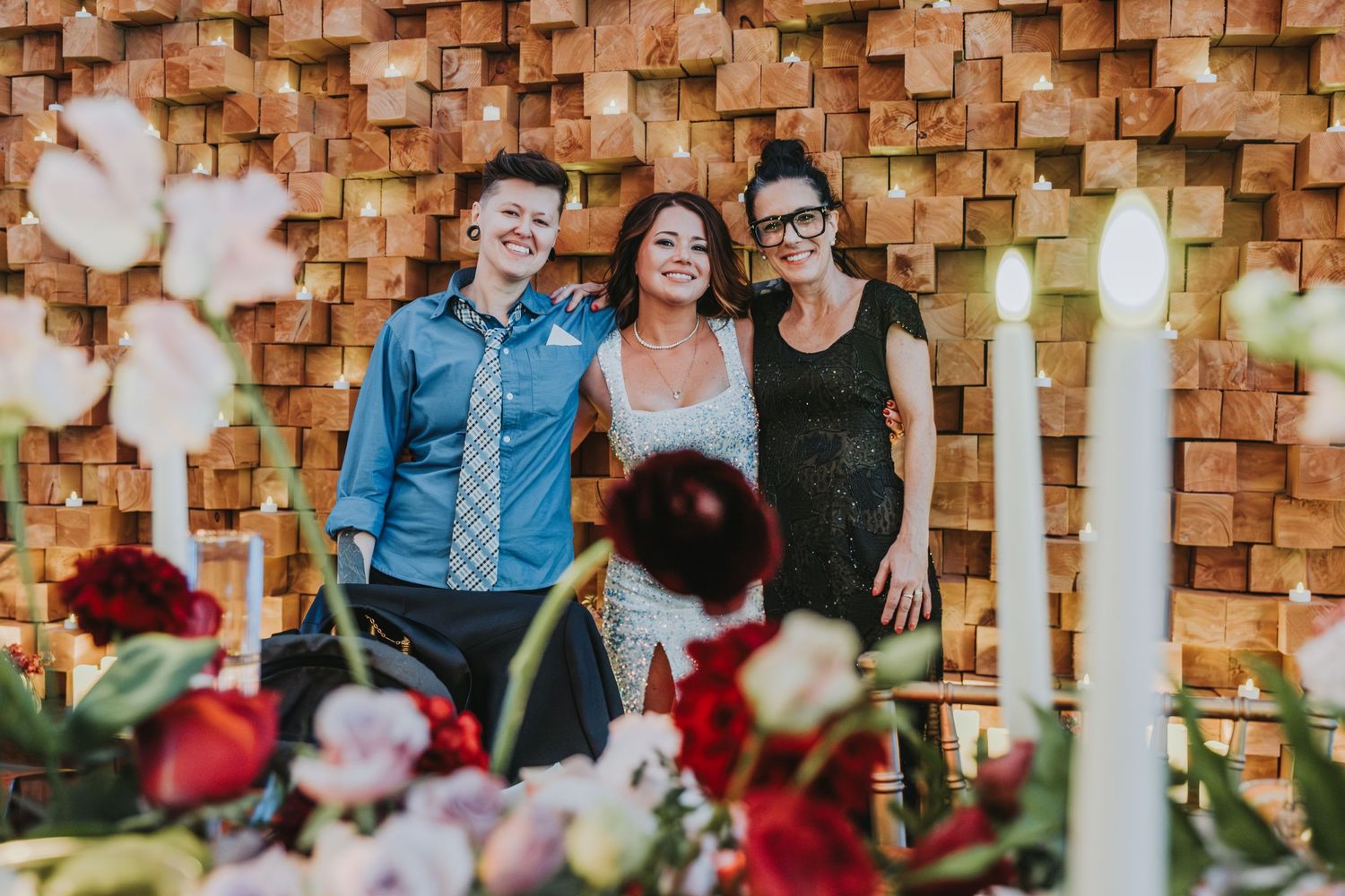 Wedding party smiles in front of wooden geometric wall with floral table decor.