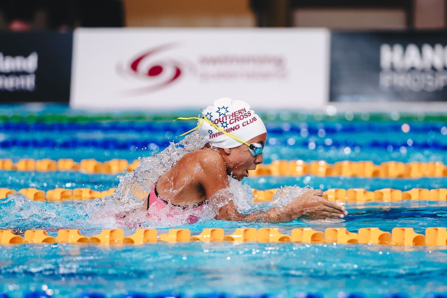 A swimmer performs breaststroke during a competitive race in a pool with multiple lanes marked by blue dividers.
