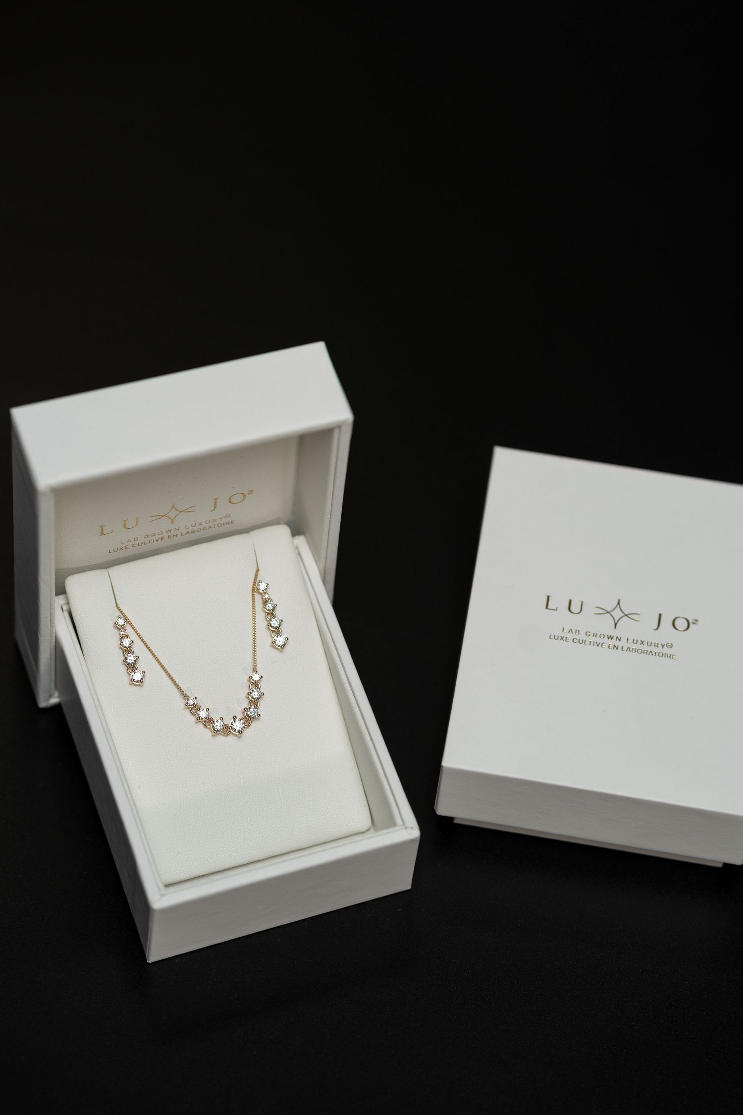 White jewelry boxes displaying delicate necklaces against a black background.