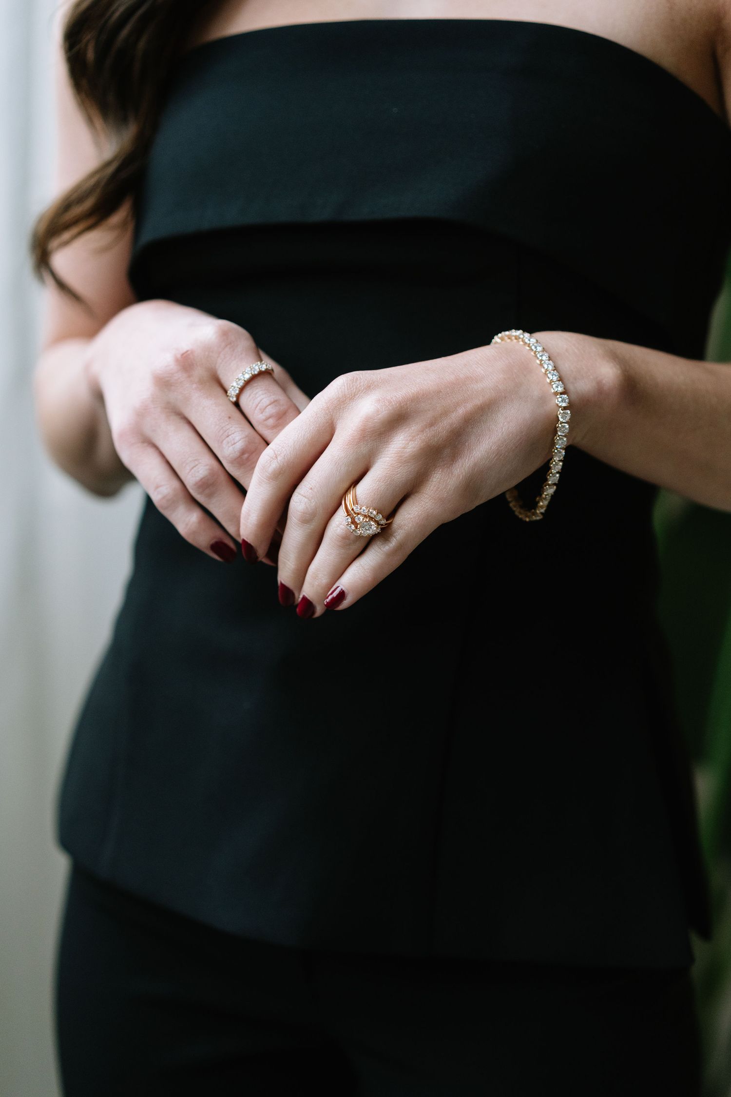 Close-up of hands wearing elegant jewelry and rings against a black dress.