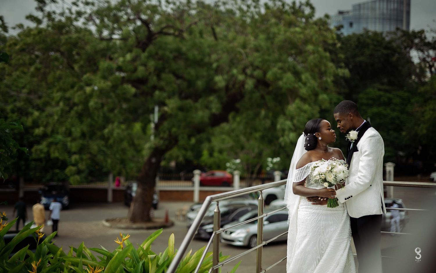 A tender moment between newlyweds embracing outdoors with lush greenery and a floral bouquet on display.