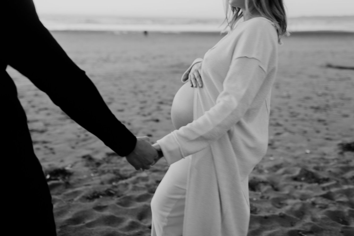 Black and white maternity photo on beach with gentle hand holding.