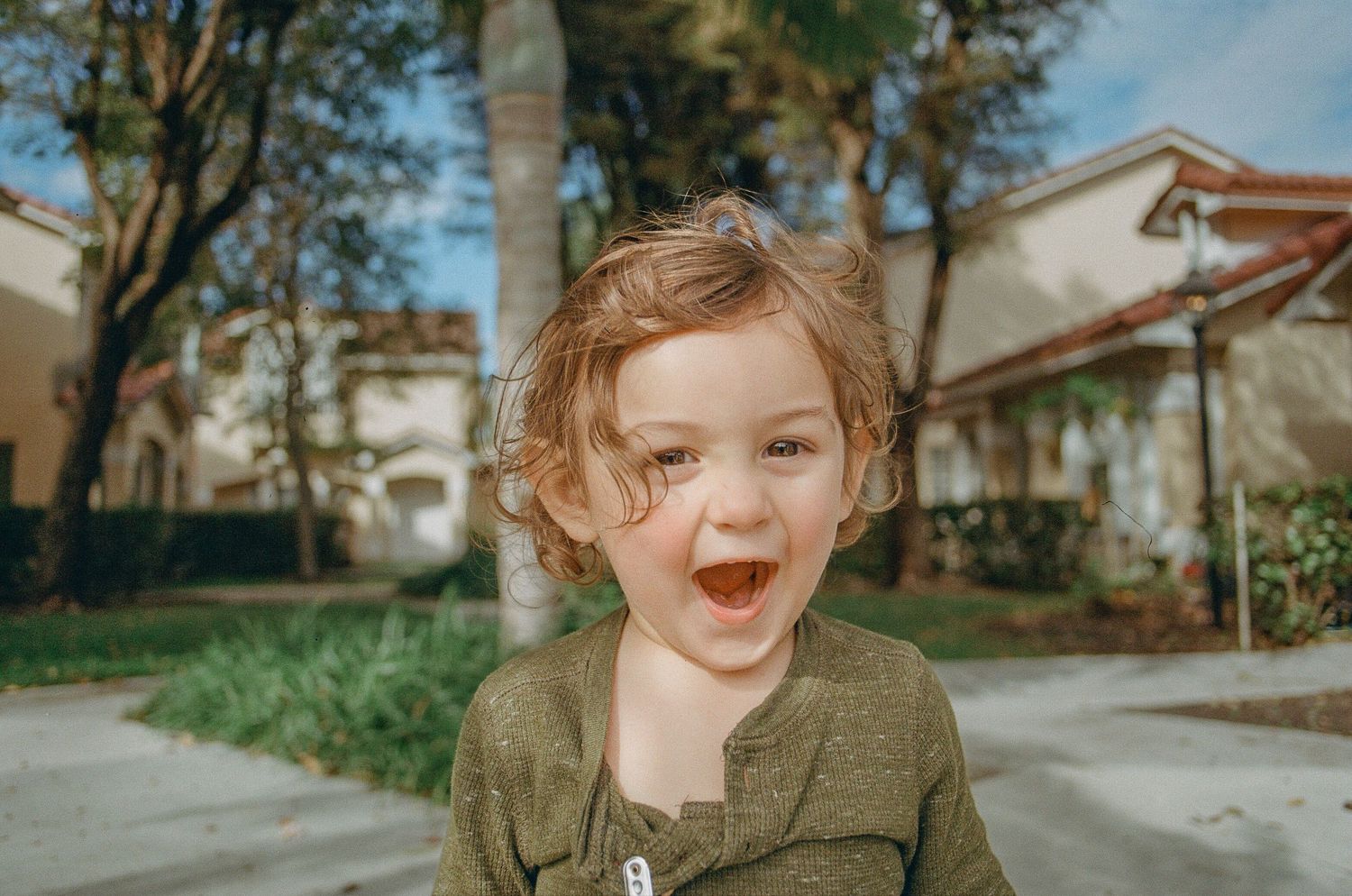 A joyful expression captured outdoors on a sunny day near suburban houses.