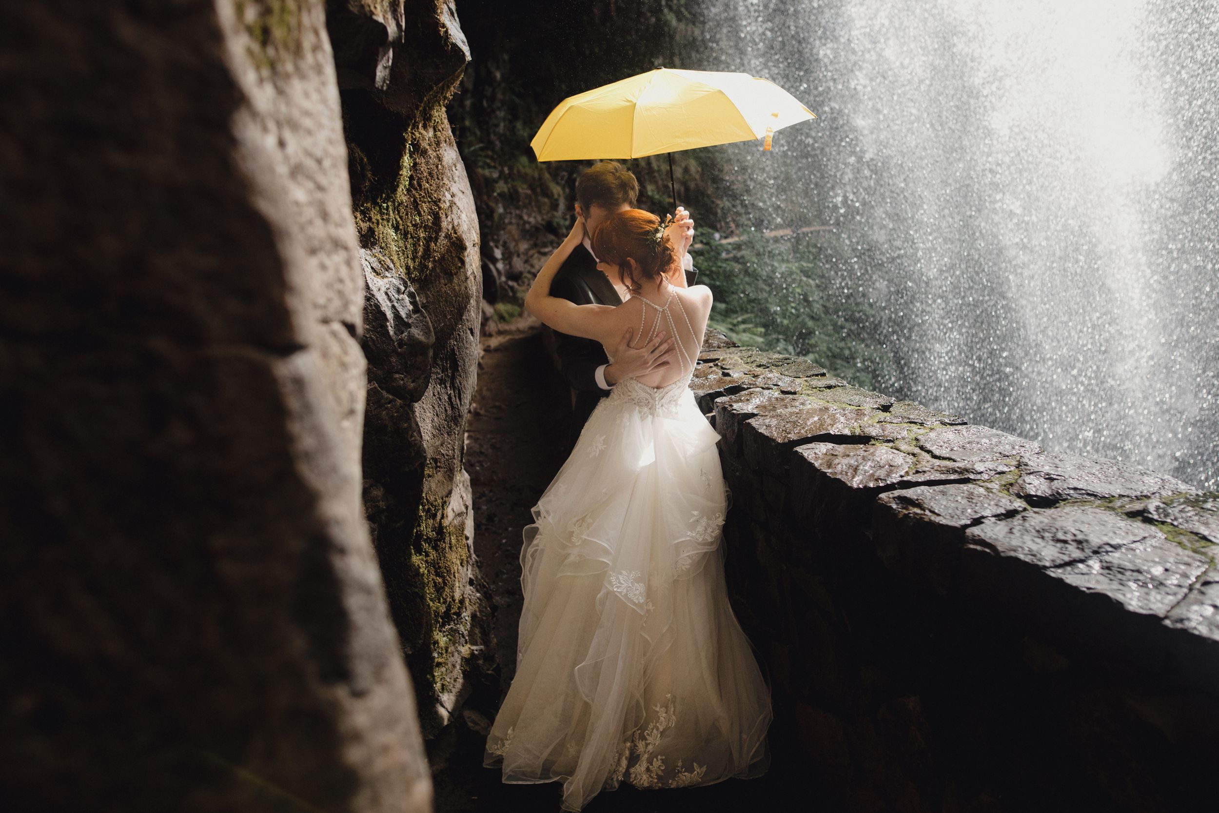 Wedding photoshoot in a rustic tunnel features a bride in a white ballgown dress and veil illuminated by natural light.
