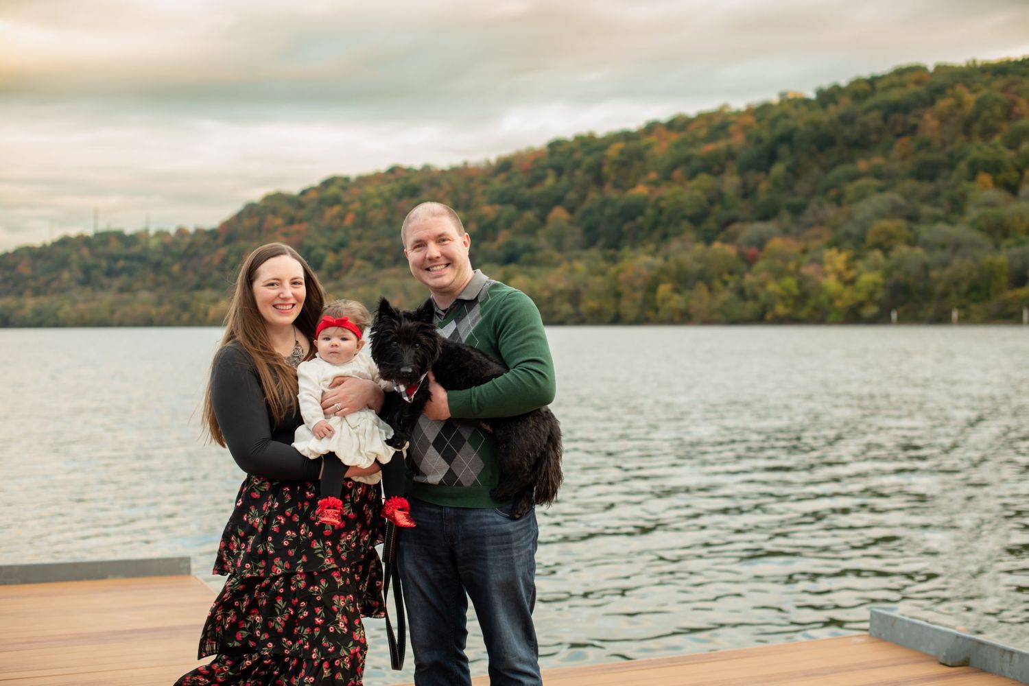 A family enjoys an autumn afternoon together on a wooden dock by a serene lake surrounded by fall foliage.