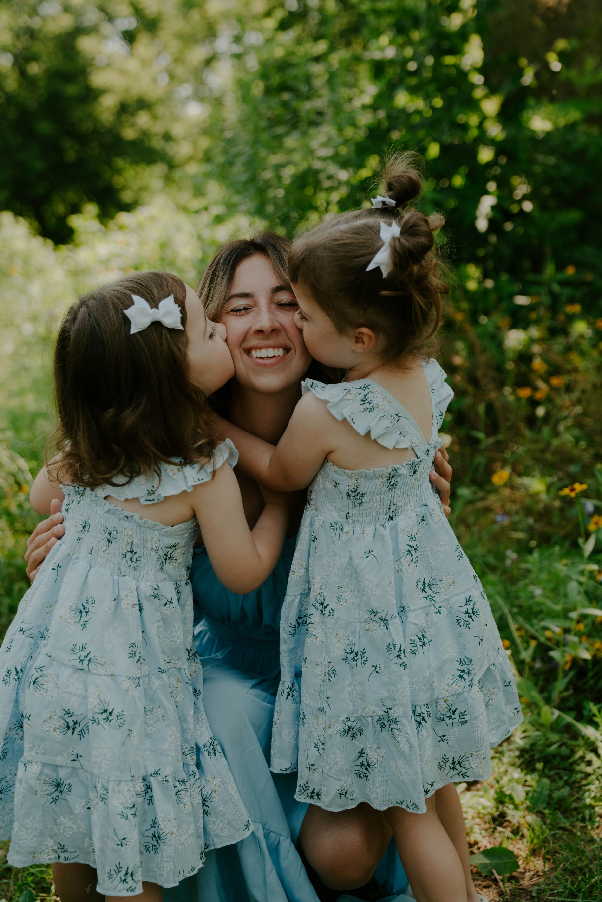 Sweet embrace between family members wearing matching floral dresses in a sunlit garden.