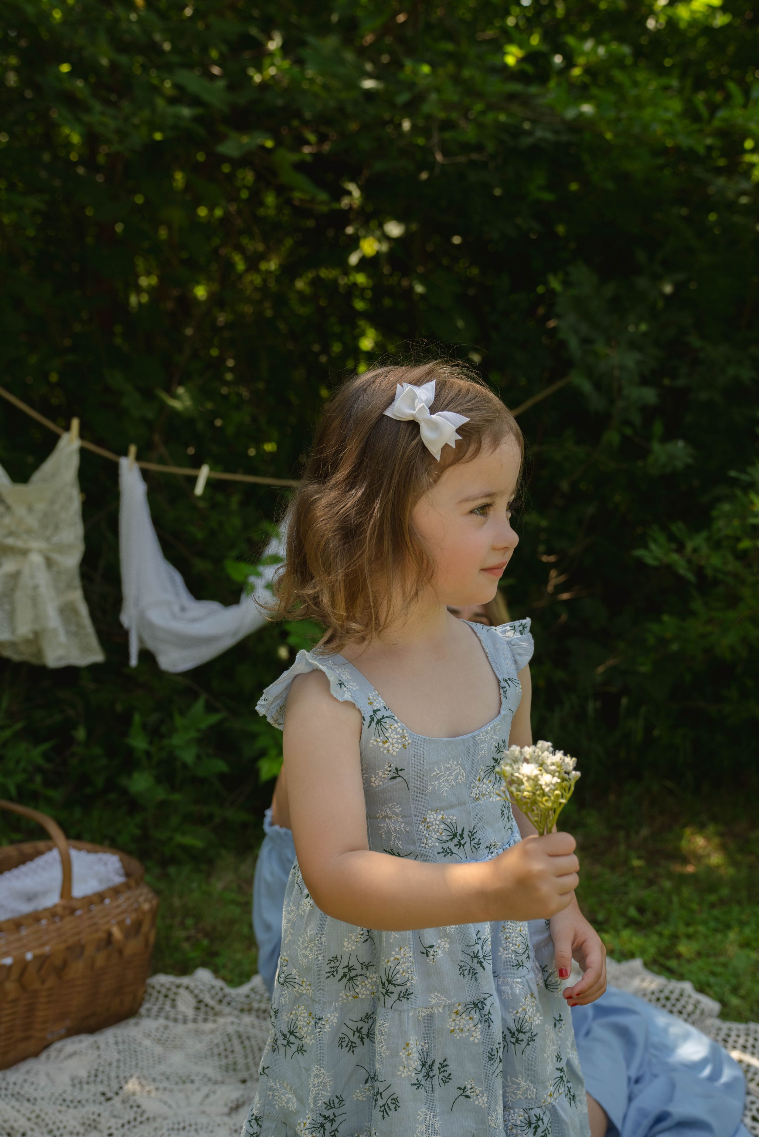 Young child in floral dress holding wildflowers with laundry line in background.