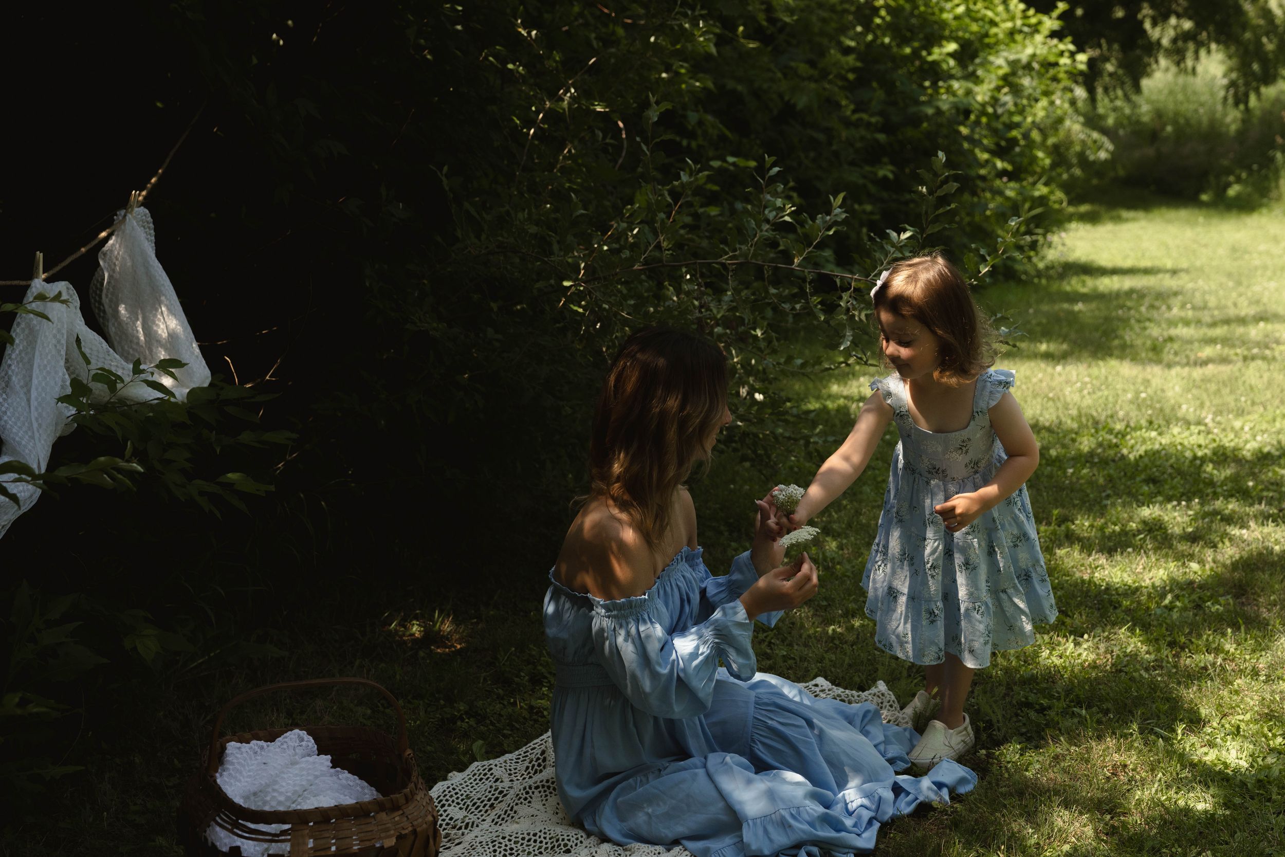 Candid outdoor moment with matching blue dresses on blanket near clothesline.