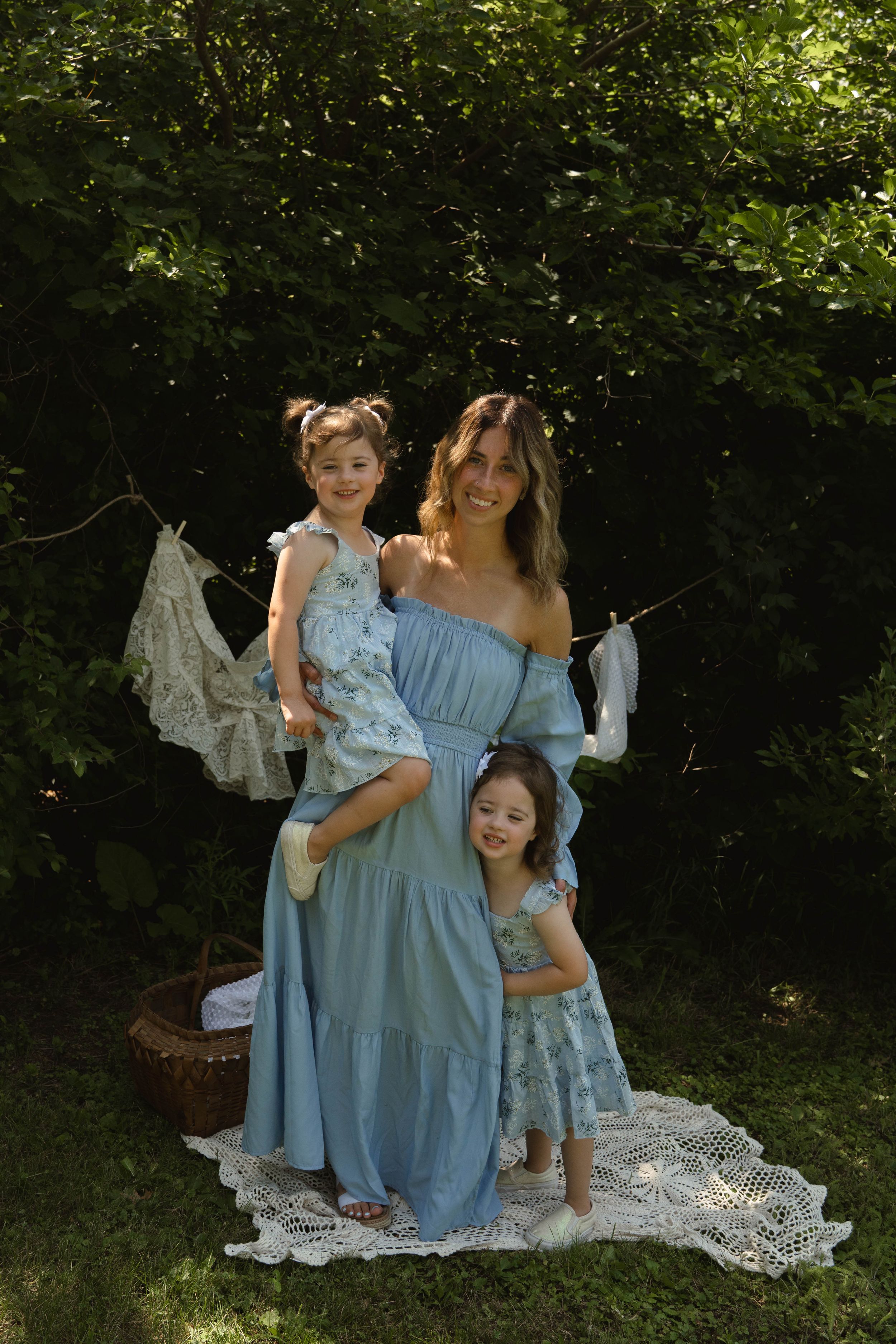 Family portrait in coordinating blue dresses against backdrop of hanging white linens.