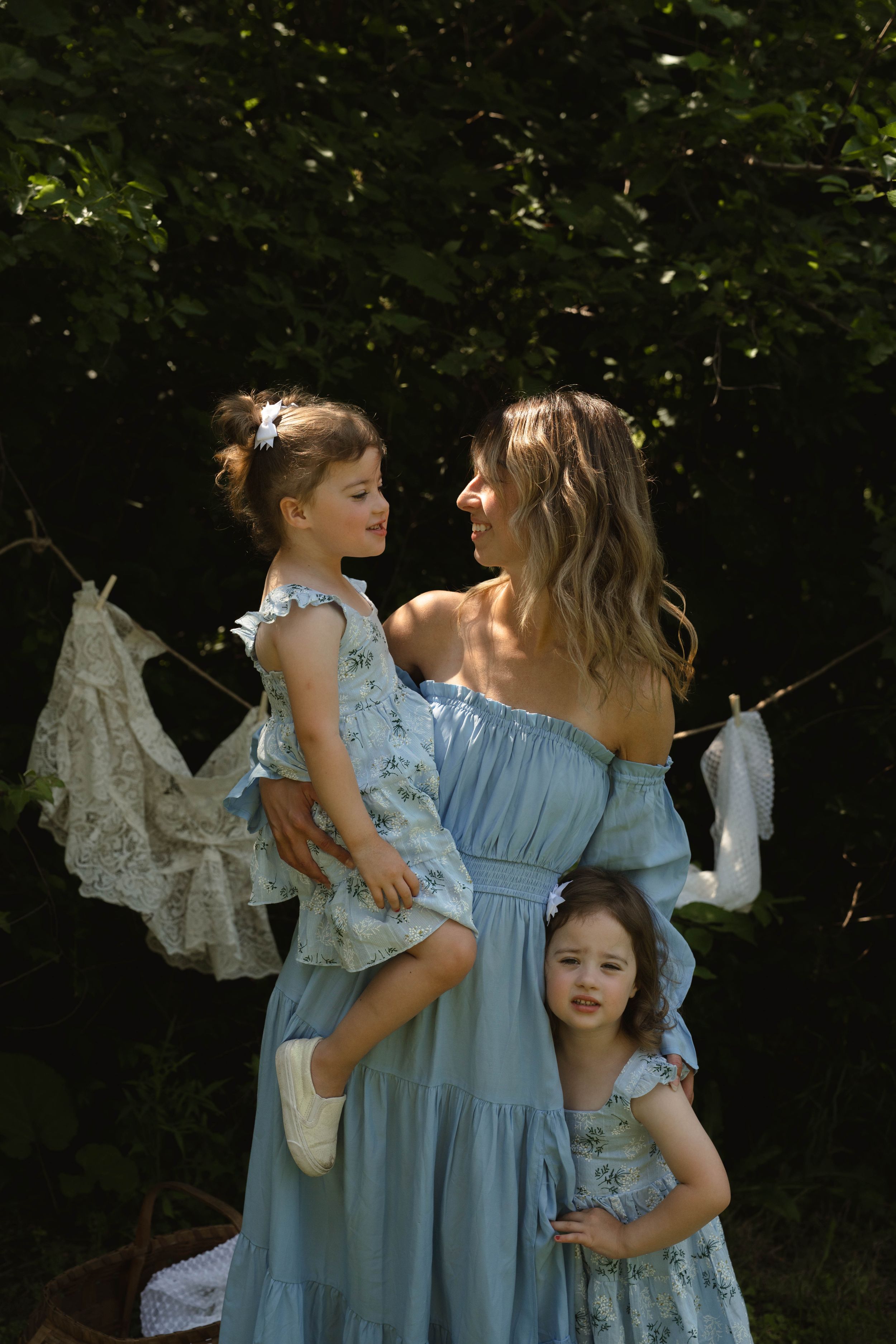 Mother and daughters wearing matching blue dresses pose together outdoors.