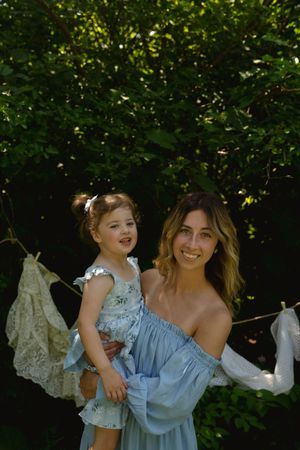 Joyful outdoor portrait with blue off-shoulder dress against hanging linens.
