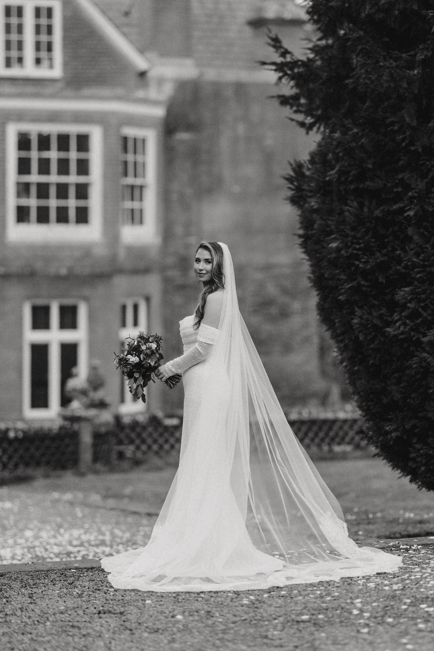 A stunning bride in a flowing white wedding dress and veil poses on stone steps surrounded by autumn leaves.