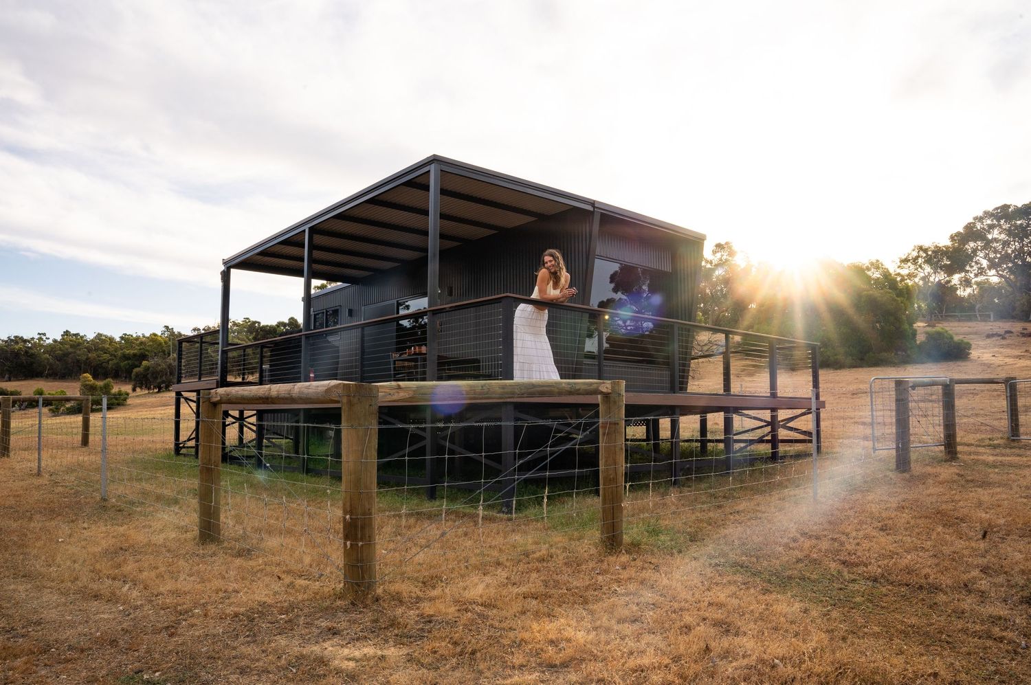 Modern elevated deck structure in rural setting with sunset backdrop.