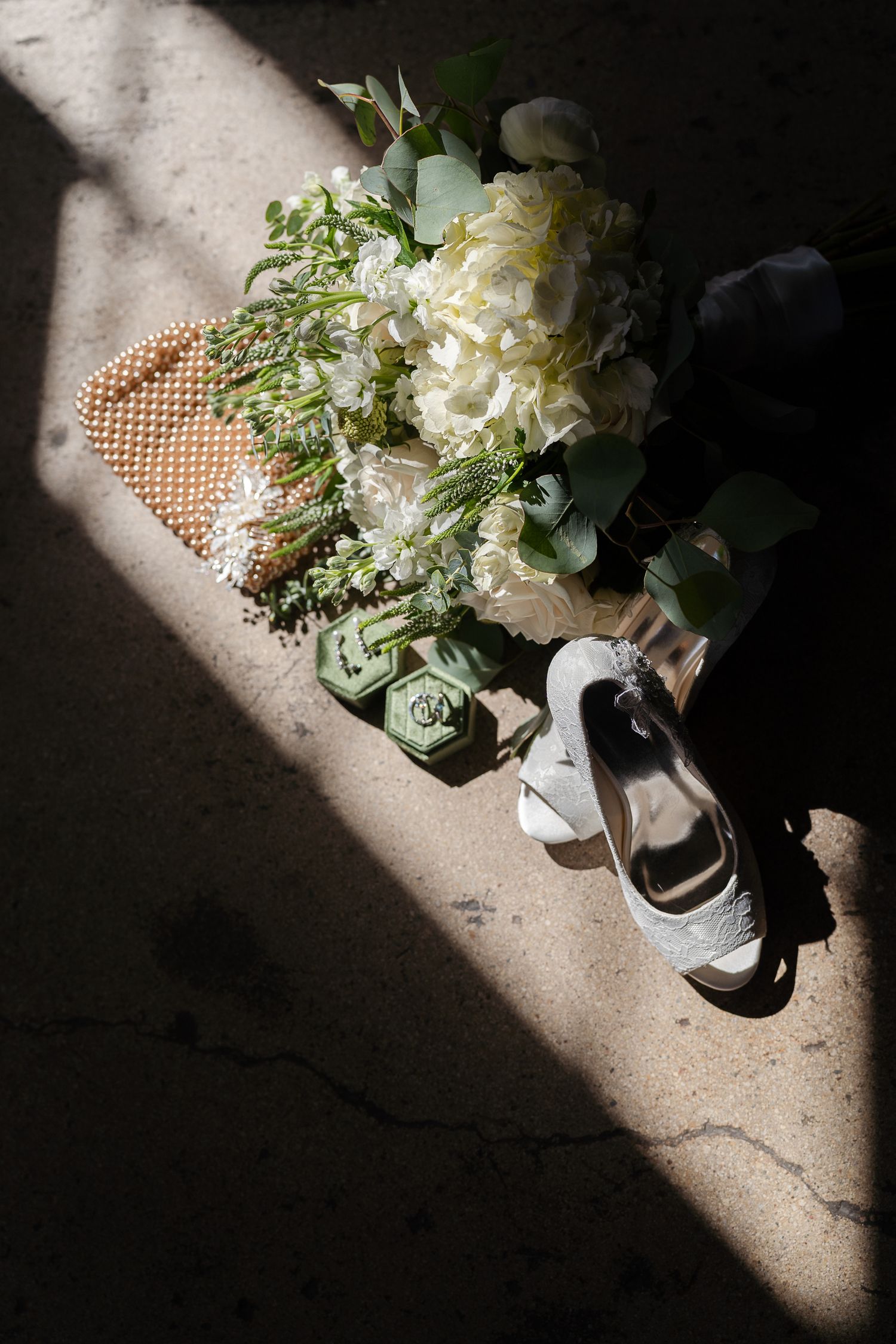 White floral bouquet with eucalyptus leaves, pearl details, and elegant bridal shoes cast in dramatic lighting and shadows.