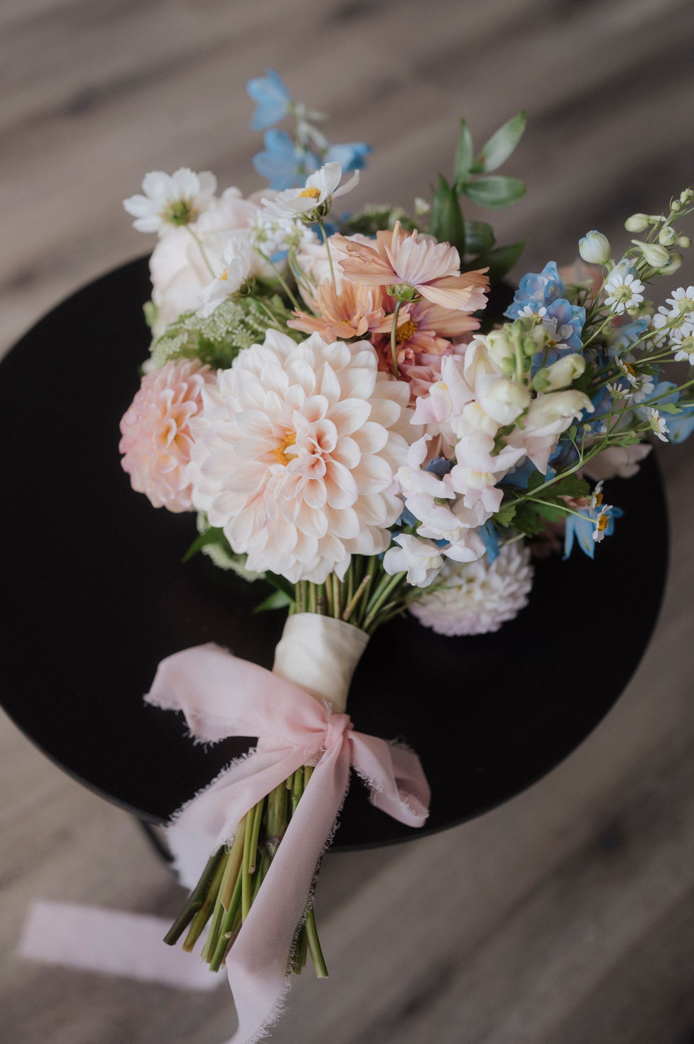 A delicate bridal bouquet with pink and white flowers tied with a silk ribbon rests on wooden boards.