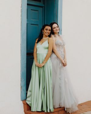 Friends in pastel dresses posing playfully by a turquoise door and white wall.
