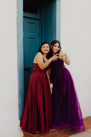 Two formal dresses in burgundy and purple showcased against white architecture.
