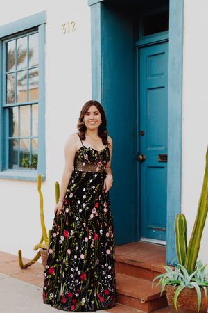 Evening gown with floral embroidery photographed against white wall and blue door.