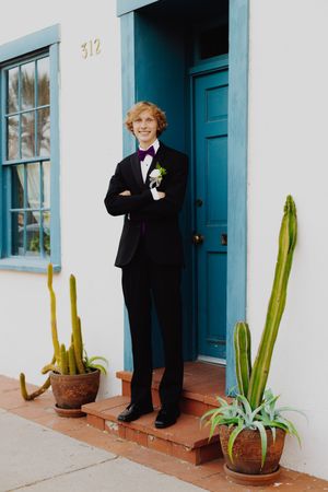 Formal black tuxedo worn in front of turquoise doorway with desert plants.