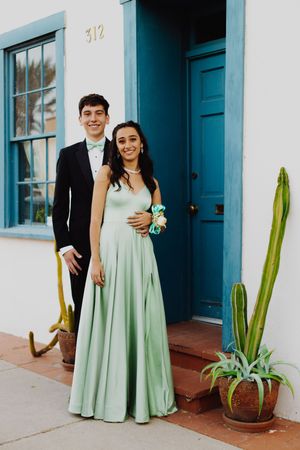 Couple in mint green dress and black tuxedo pose by turquoise door with cactus.
