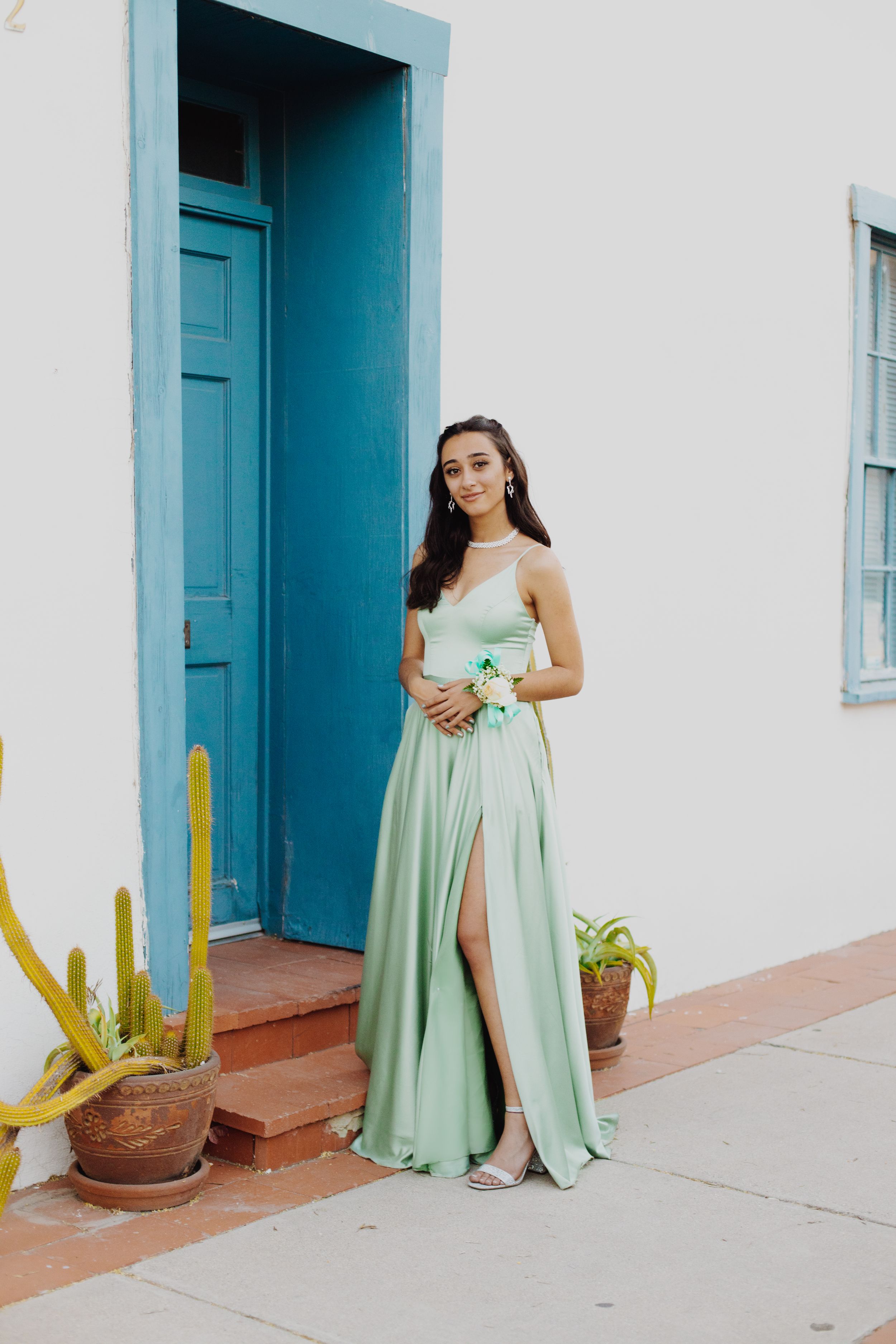 Elegant mint green formal dress with slit photographed against white wall and blue door.