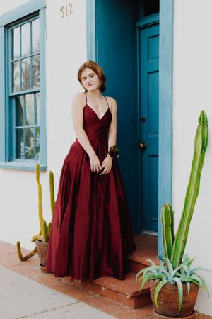 Burgundy v-neck formal gown posed against white wall with turquoise door frame.