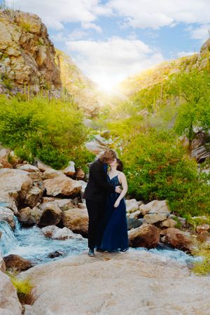 A romantic photo session by a rushing stream in a mountainous landscape with rocky outcrops and green foliage.