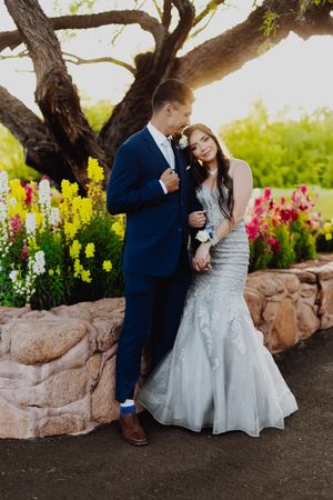 Formal couple poses romantically against a tree with vibrant flowers in the background.