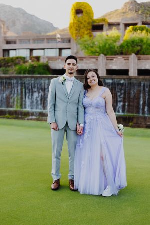 Couple in formal wear stands on a golf course with a waterfall and mountain backdrop.