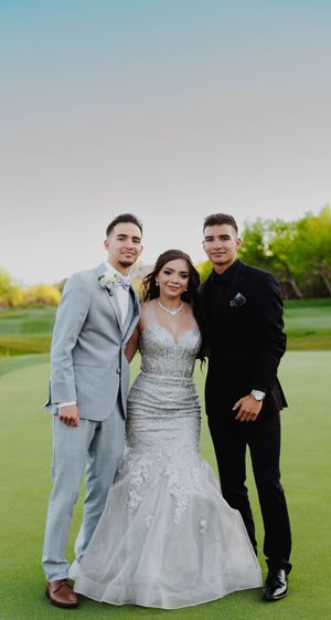 Three people in formal attire pose together on a manicured golf course at sunset.