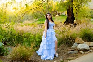 Woman in light blue dress poses in natural outdoor setting during golden hour.