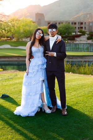 Couple in formal wear taking photos on green lawn with mountain views.