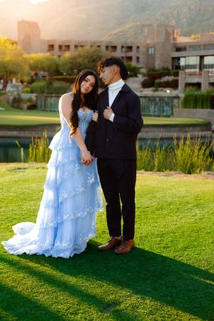Couple in formal attire embracing on golf course during sunset photo session.