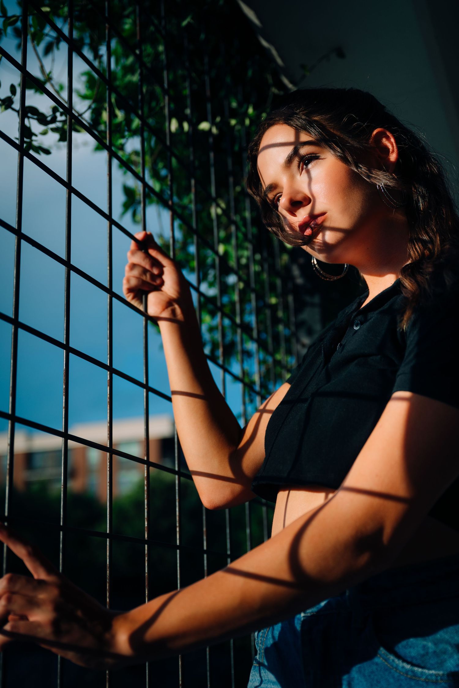 Artistic portrait with dramatic shadows cast through metal fence during blue hour.