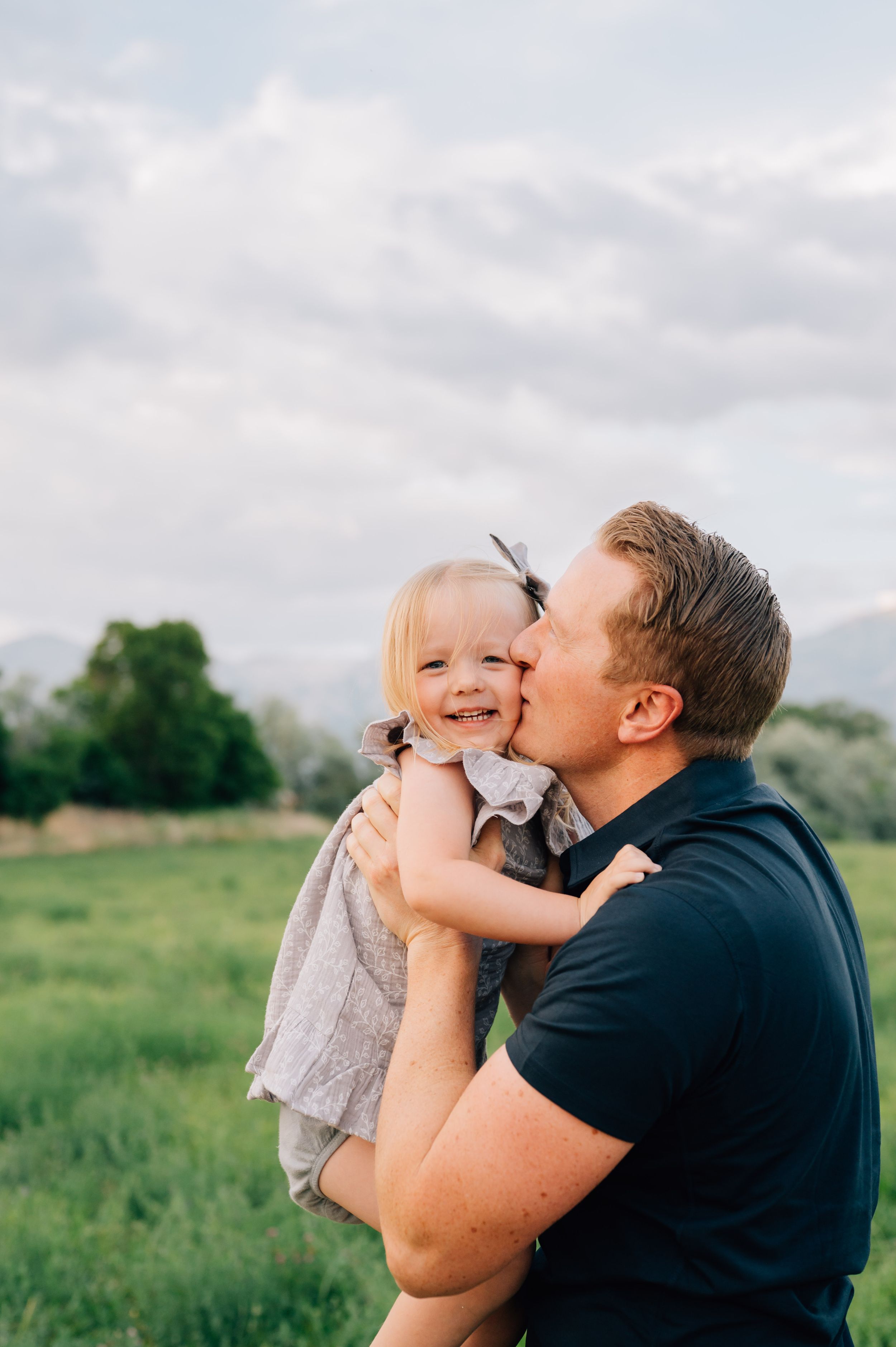 A tender moment captured between a parent and child embracing in a sunny meadow with mountains visible.