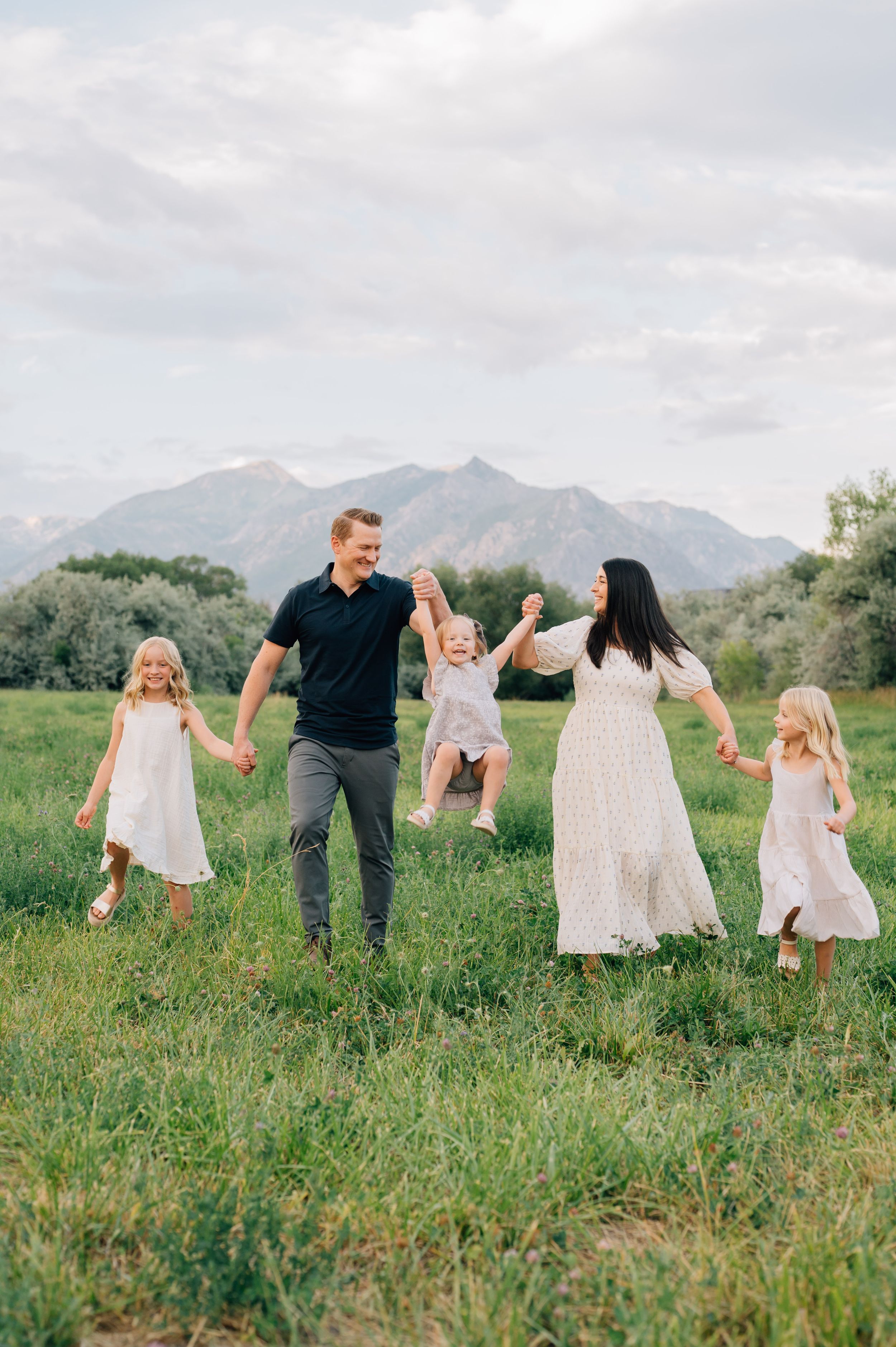 A family enjoys a playful moment together in a green meadow with mountains in the background.