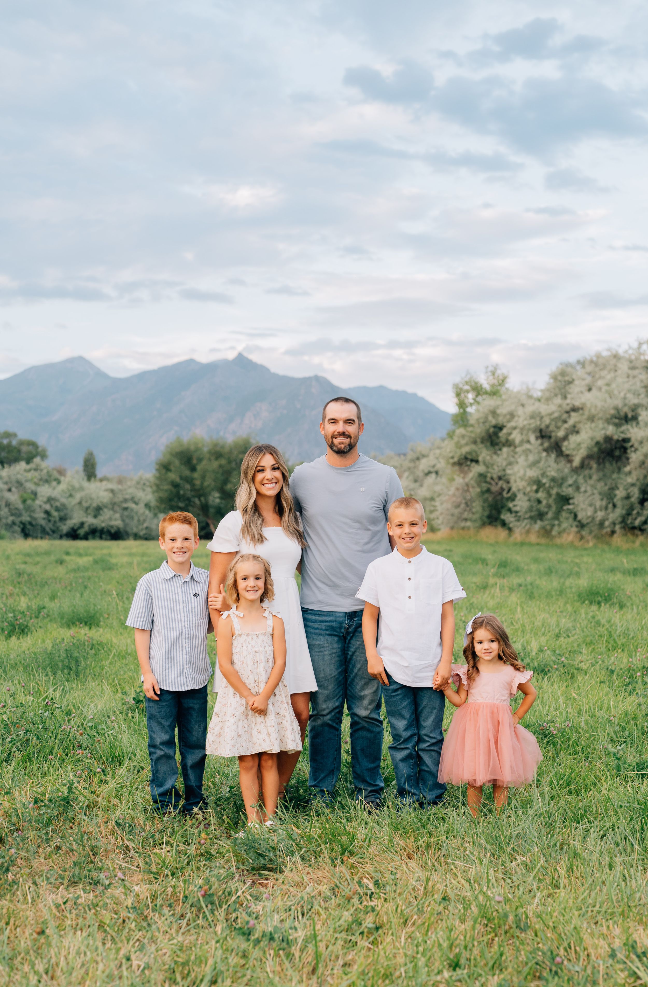 Family portrait of parents and children standing together in front of mountain scenery on a summer day.